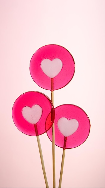 Three round lollipops with a heart on a pink background Vertical banner for Valentines Day