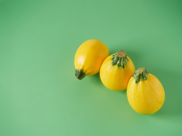 Three round yellow zucchini in a row on a plain green background