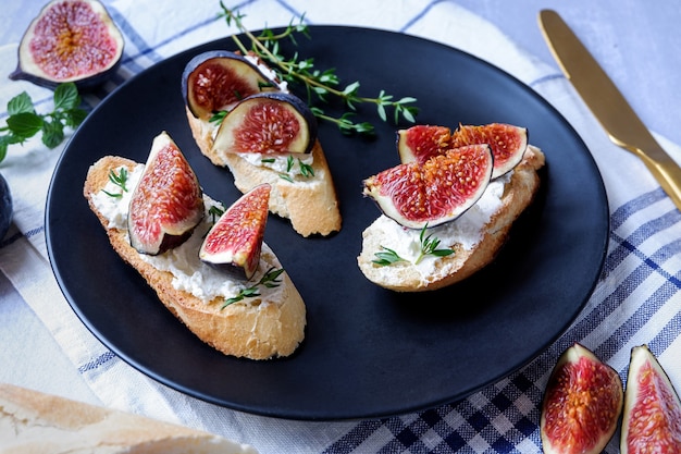 Three sandwiches with goat cheese, fig and thyme served on a black plate on light grey surface