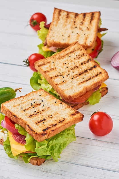 Three sandwiches with ham, lettuce and fresh vegetables on a white background