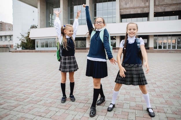 Photo three schoolgirls in uniform in skirts and golfs rejoice at the end of lessons.