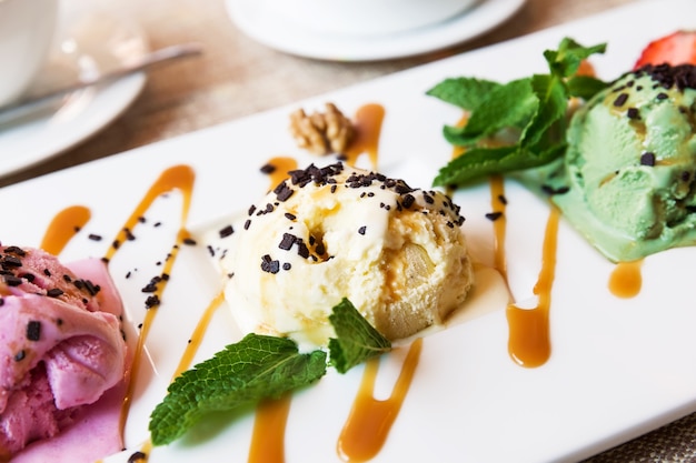 Three scoops of pistachio, strawberry and vanilla ice cream in bowl in cafe