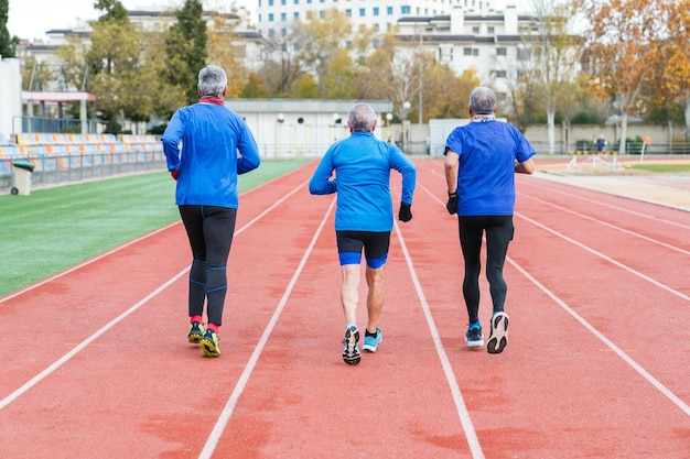 青いスポーツウェアを着た3人のシニア男性ランナーがアクティブなライフスタイルを示すアスリートコースでトレーニングしています