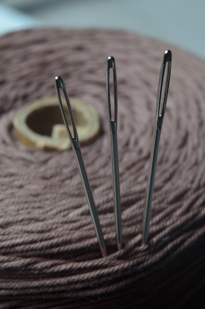 Three sewing needles are inserted into a spool of thread. close-up.