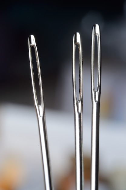 Three sewing needles on the background of many multi-colored babinets. needle eye. macro.