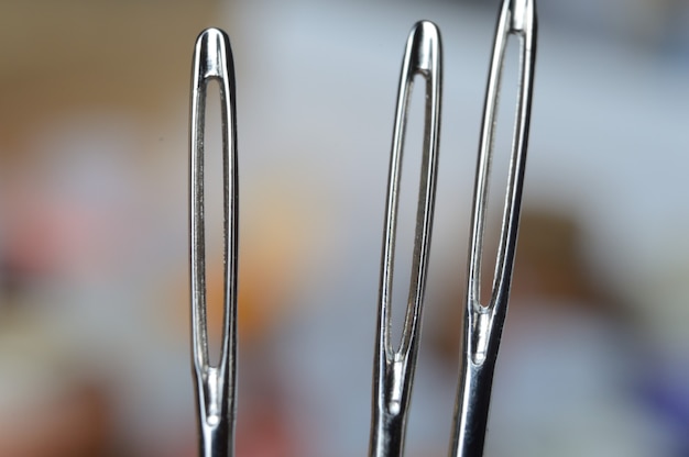 Three sewing needles on the background of many multi-colored babinets. needle eye. macro.