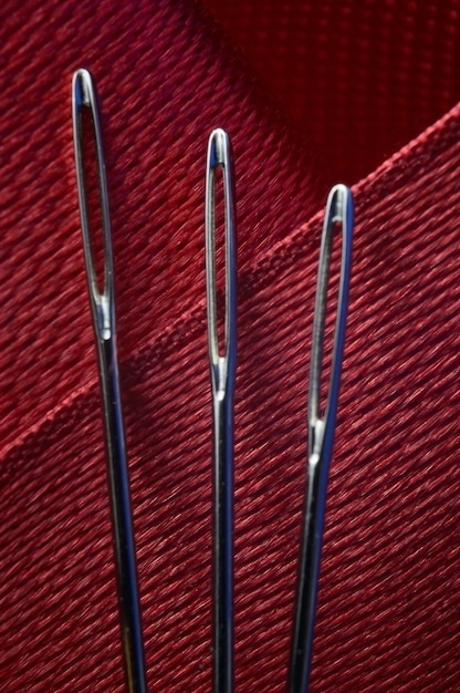 Three sewing needles on a red fabric background. close-up.