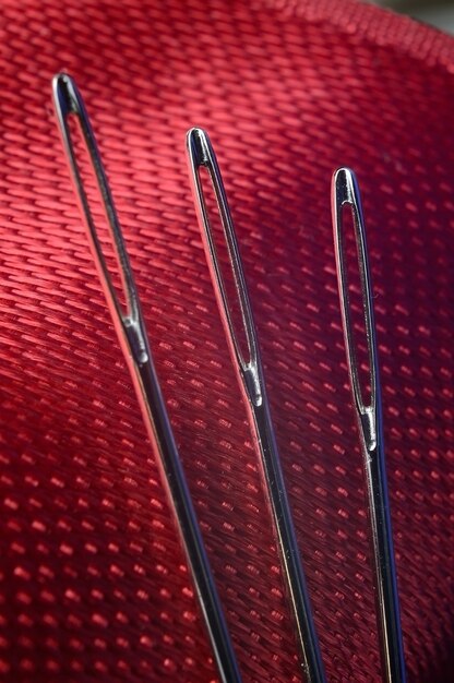 Three sewing needles on a red fabric background. close-up.