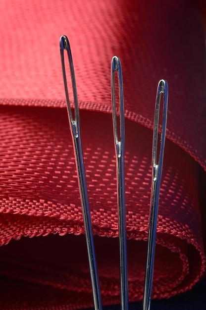 Three sewing needles on a red fabric background. close-up.