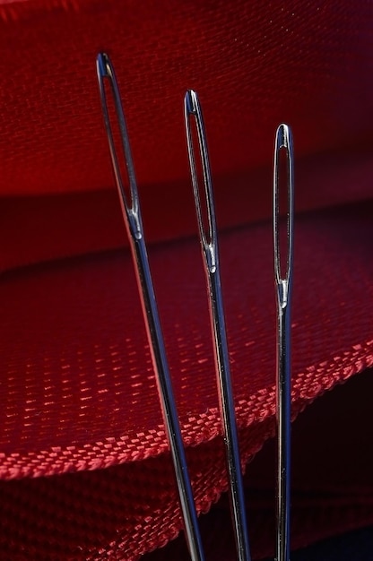 Three sewing needles on a red fabric background. close-up.