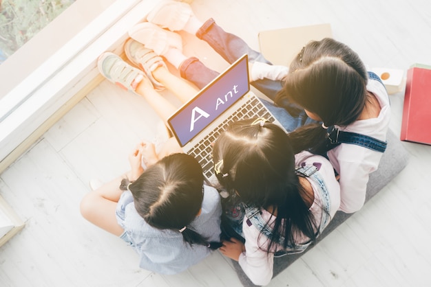 写真 3人の姉妹が床に横になってラップトップを使って学業をしています。