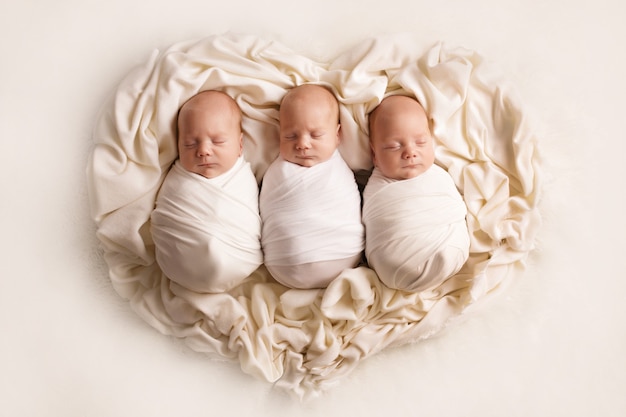 Three sleeping newborn brothers on the background of the heart. High quality photo