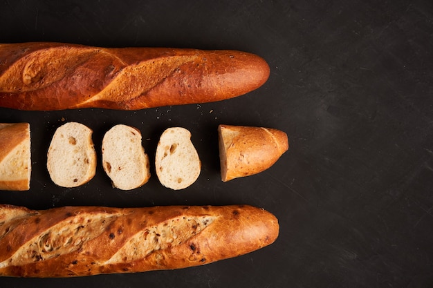 Tre baguette francesi croccanti affettate si trovano sullo sfondo del tavolo nero scuro semi di sesamo pasticcini nazionali francesi classici