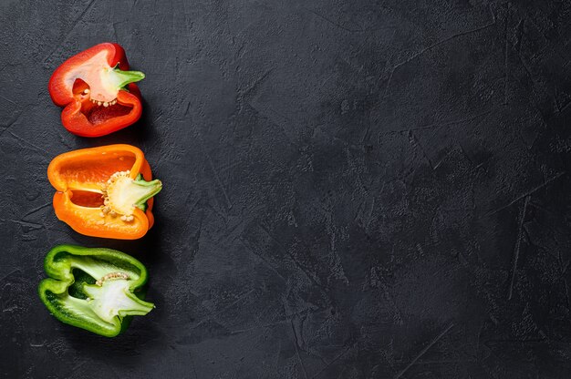 Three sliced orange, green and red bell peppers. Black background. Top view. Space for text