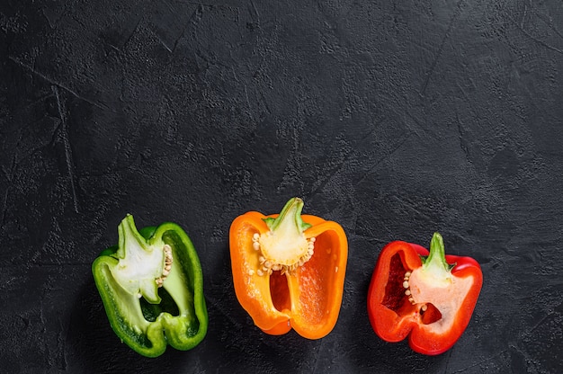 Three sliced orange, green and red bell peppers. Black background. Top view. Space for text