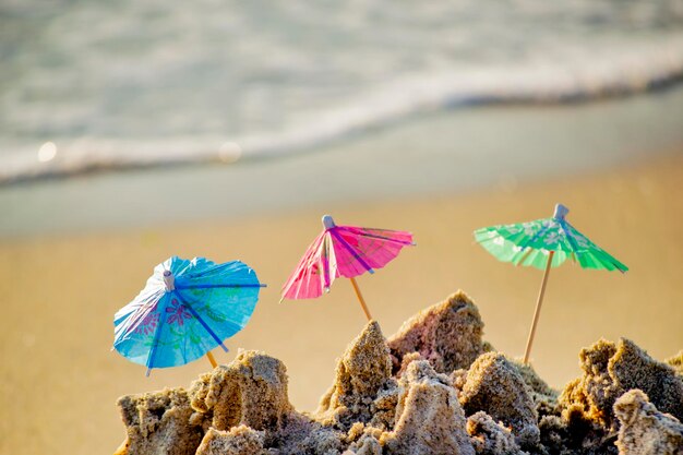 Three small beach umbrellas made of paper for cocktail stand in sand