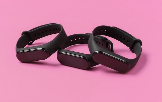 Three smart bracelets on pink background. Modern gadgets for sports and everyday activities