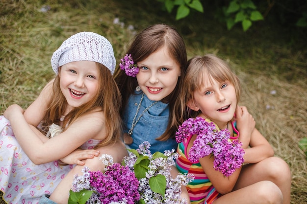 Photo three smiling european girls sit in a garden on the ground with lilac flowers top view