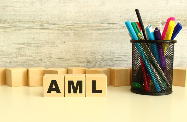 Three stacked wooden cubes with letters AML on a white desktop on a gray background.