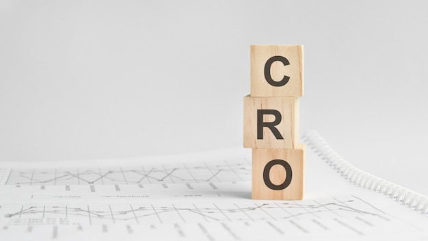 Three stone cubes on the background of white financial statements, tables with the word CRO - acronim Conversion Rate Optimization. Strong business concept. Gray background.