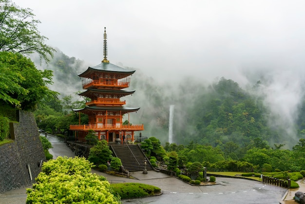 Three-story Sanjudo pagoda of Seiganto-ji temple with Nachi falls and beautiful foggy scenery in the background , listed as a UNESCO World Heritage Site in Wakayama Prefecture , Japan