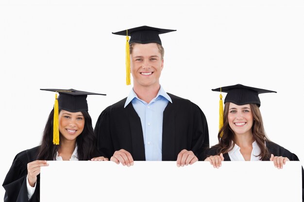 Three students having graduated holding a blank poster