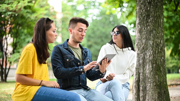 Tre studenti che studiano insieme a una tavoletta digitale seduti su una panchina all'aperto