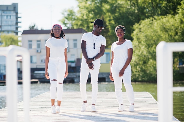 Tre eleganti amici afroamericani, indossano abiti bianchi. la moda di strada dei giovani neri. uomo di colore con due ragazze africane poste.