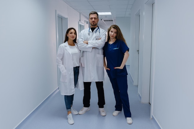 Three successful doctors are standing in the hallway and looking into the camera Two female and male colleagues