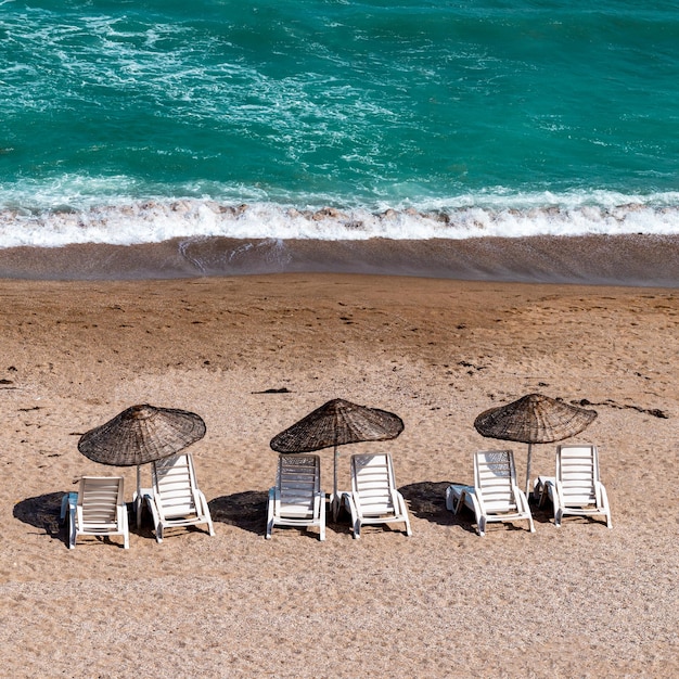 Three sunbed and umbrellas on the beach with clear blue sea holiday tourism and summer theme