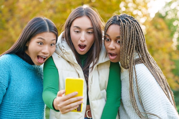 Three surprised friends using a mobile outdoors