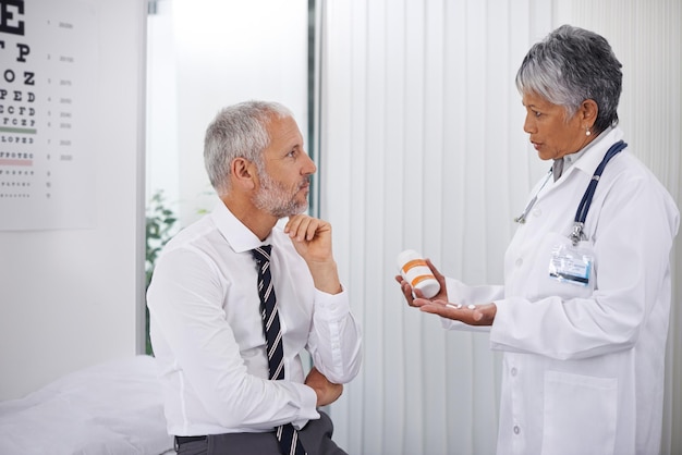 Три таблетки два раза в день Зрелый врач дает пузырек с таблетками одному из своих пациентов во время осмотра