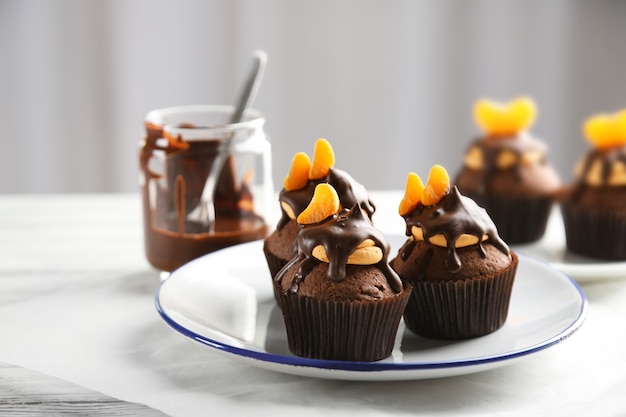 Three tasty cupcakes with slice of mandarin and chocolate on a plate, close up