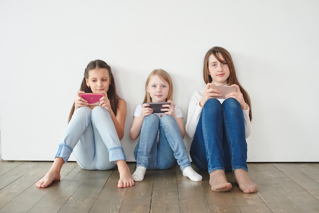 写真 電話でゲームをしている白い背景の上の3人の10代の少女。ギャンブル依存症