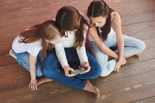 Three teenage girls on a pink background playing games on the phone. Gambling addiction