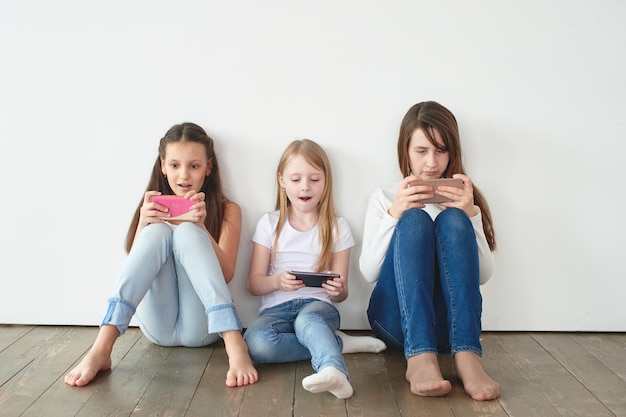 Three teenage girls on a white background playing games on the phone. Gambling addiction