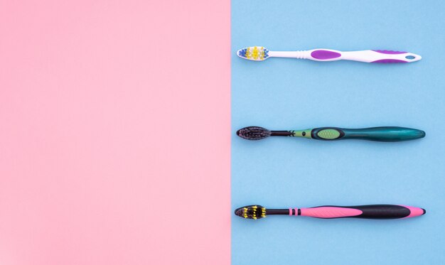 Three toothbrushes are isolated on blue and pink for copyspace. Flat lay Care Concept.