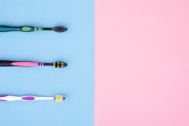 Three toothbrushes are isolated on blue and pink for copyspace. Flat lay