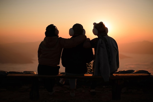 Three tourists are sitting on the top of the mountain watching the sun rise