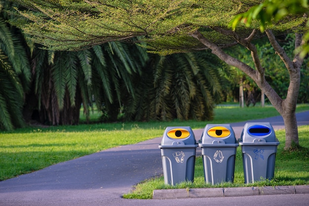 Three trashcans in a park with green tree and plants in public park