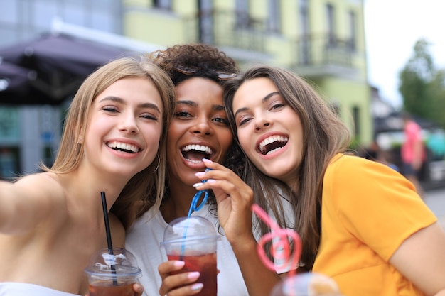 Foto tre ragazze alla moda cool hipster, amici bevono cocktail sullo sfondo urbano della città.