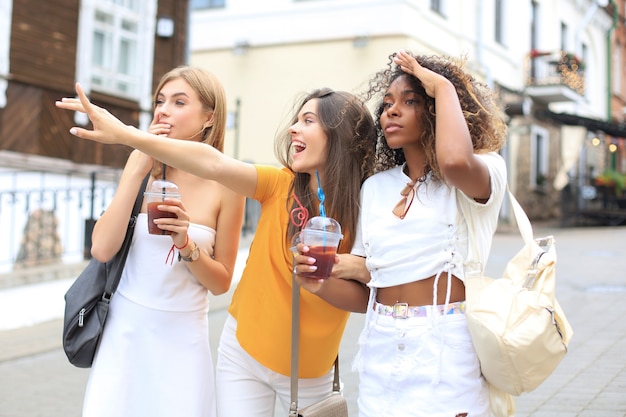 Three trendy cool hipster girls, friends drink cocktail in urban city background.