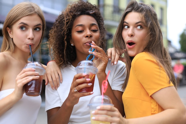 Foto tre ragazze cool hipster alla moda, amici bevono cocktail sullo sfondo urbano della città.