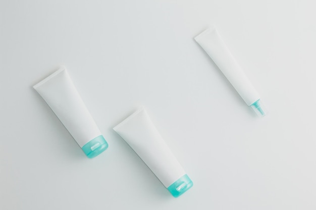 Three turquoise and white cosmetic tube mockups on white background Flat lay