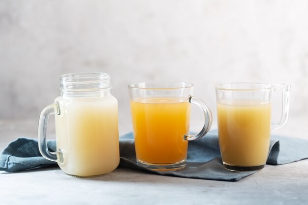 Three types of Homemade Beef Bone Broth in Glasses on a gray space