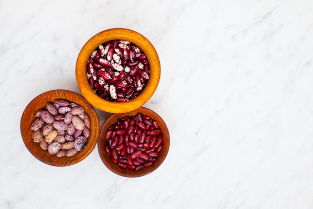 Three types of kidney beans in wooden bowls on a white background