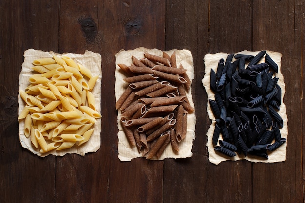 Three types of penne pasta on a wooden table