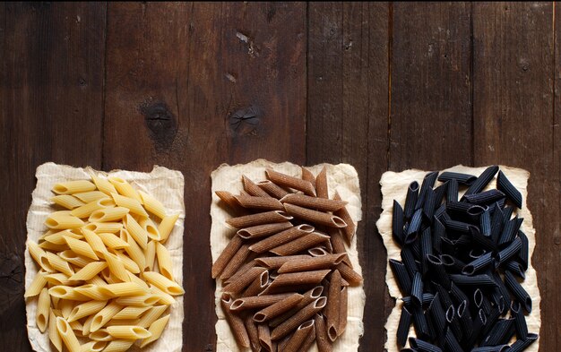 Three types of penne pasta on a wooden table