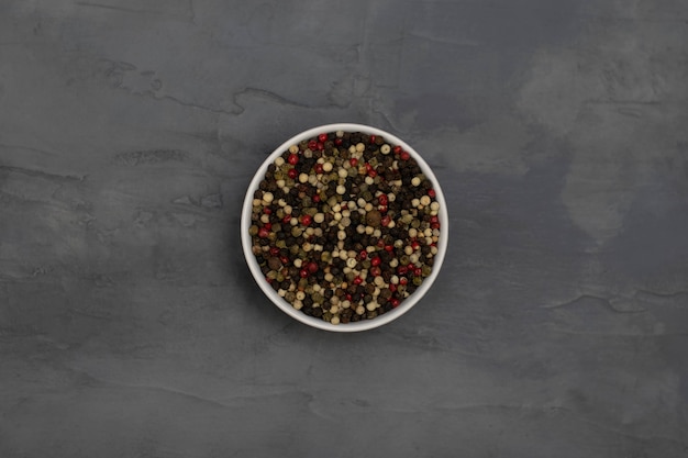 Three types of pepper, white, black and red in a white bowl on a gray stone background. Top view.