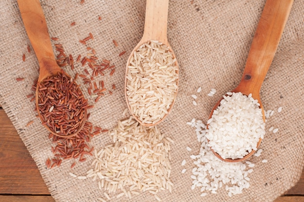 Foto tre tipi di riso in riso marrone, rosso e rotondo del cucchiaio di legno su fondo di legno
